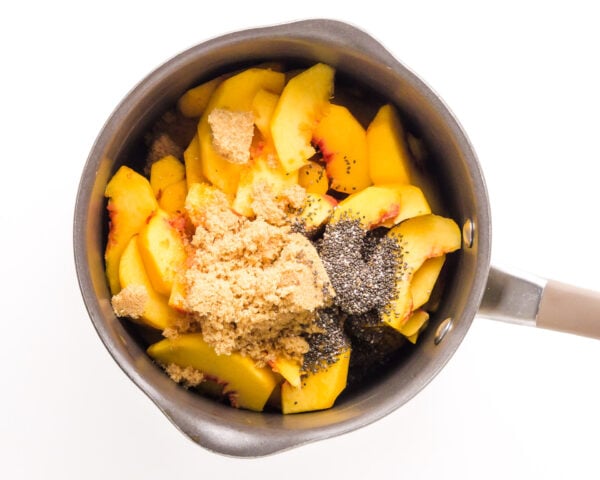 Peaches are topped with brown sugar and chia seeds in a saucepan.