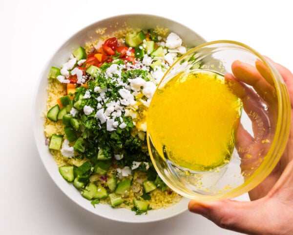 Salad dressing is being poured over a salad with lots of veggies.