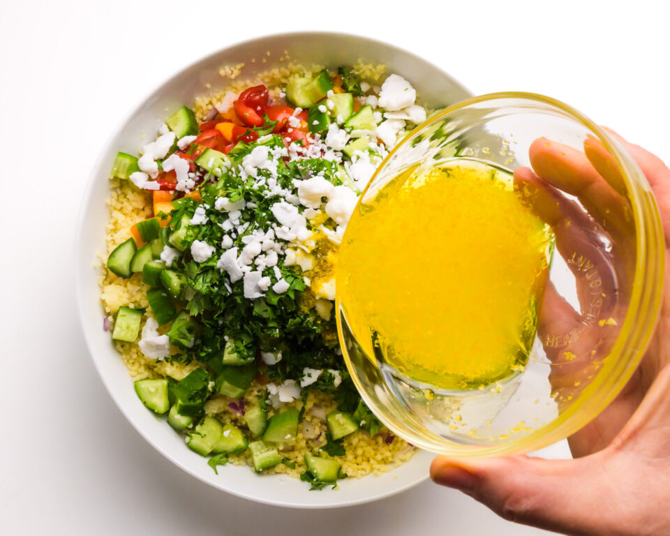 Salad dressing is being poured over a salad with lots of veggies.