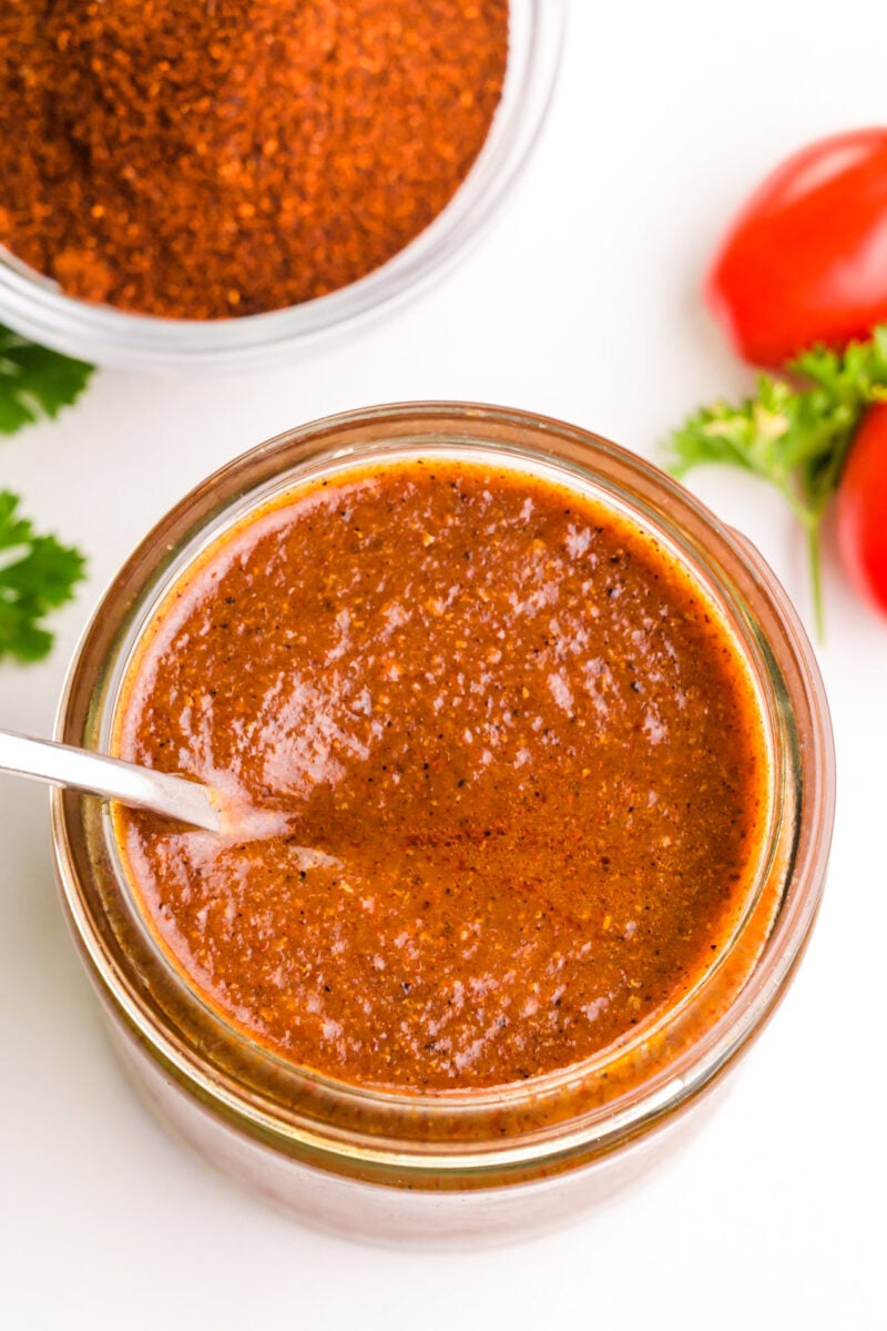 Looking down on a glass jar of enchilada sauce with a spoon in it.