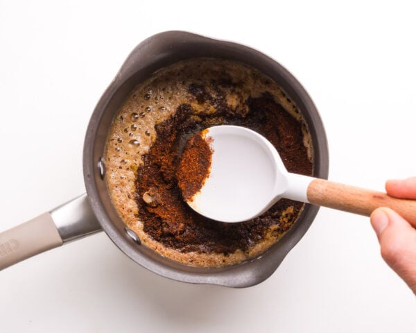 A hand holds a spatula, stirring ingredients in a saucepan.