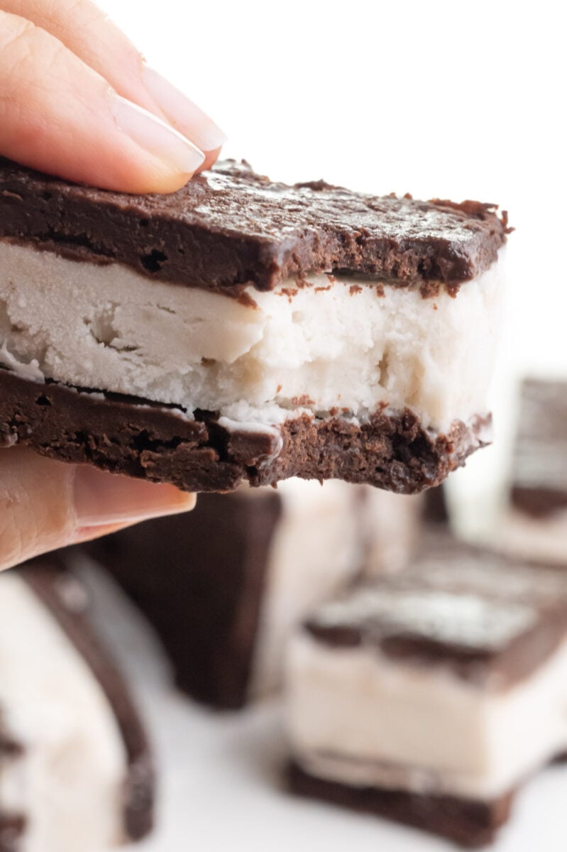 A hand holds a plant-based ice cream sandwich with a bite taken out.