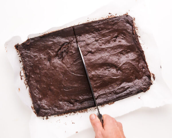 A knife cuts a long rectangle chocolate cookie in half.