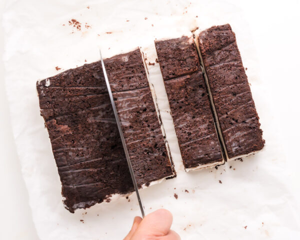 A knife is being used to cut big blocks of ice cream sandwiches into smaller sandwiches.