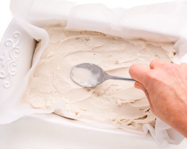 Vanilla ice cream is being spread in a pan lined with parchment paper.