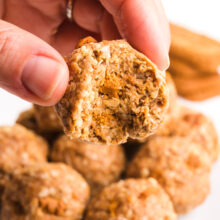 A hand holds a Biscoff ball with a bite taken out, hovering over a plate with more of the treats.