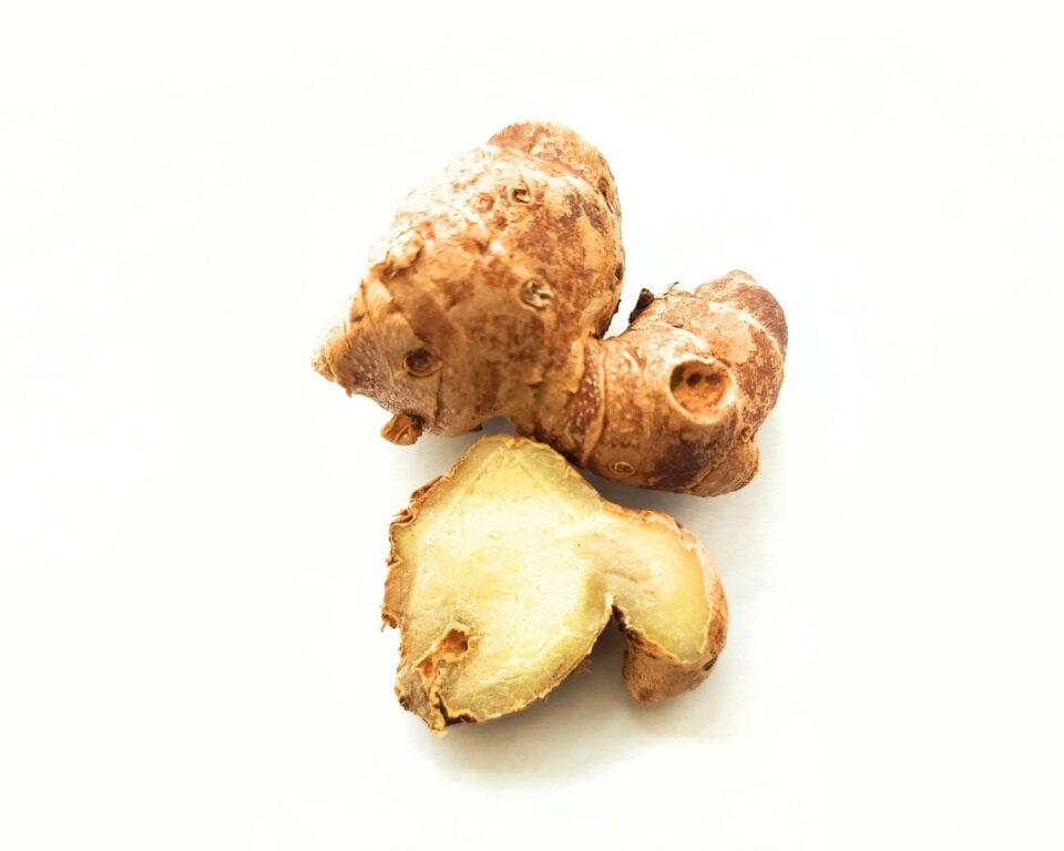 Two kencur roots are on a table. One has been cut in half to reveal the white flesh inside.