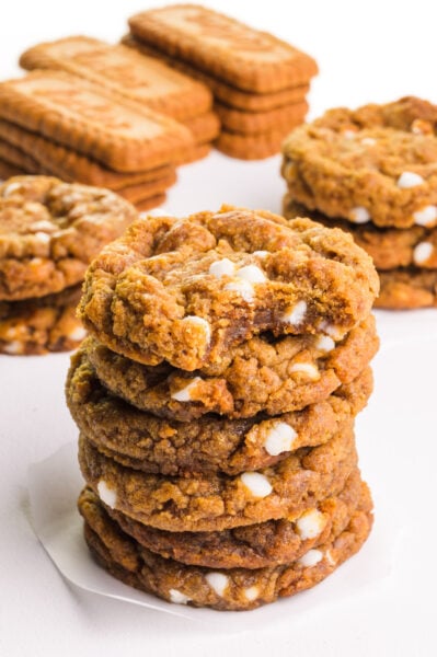 A stack of cookies has a bite taken out of the top one. There are more cookies and biscoff cookies in the background.