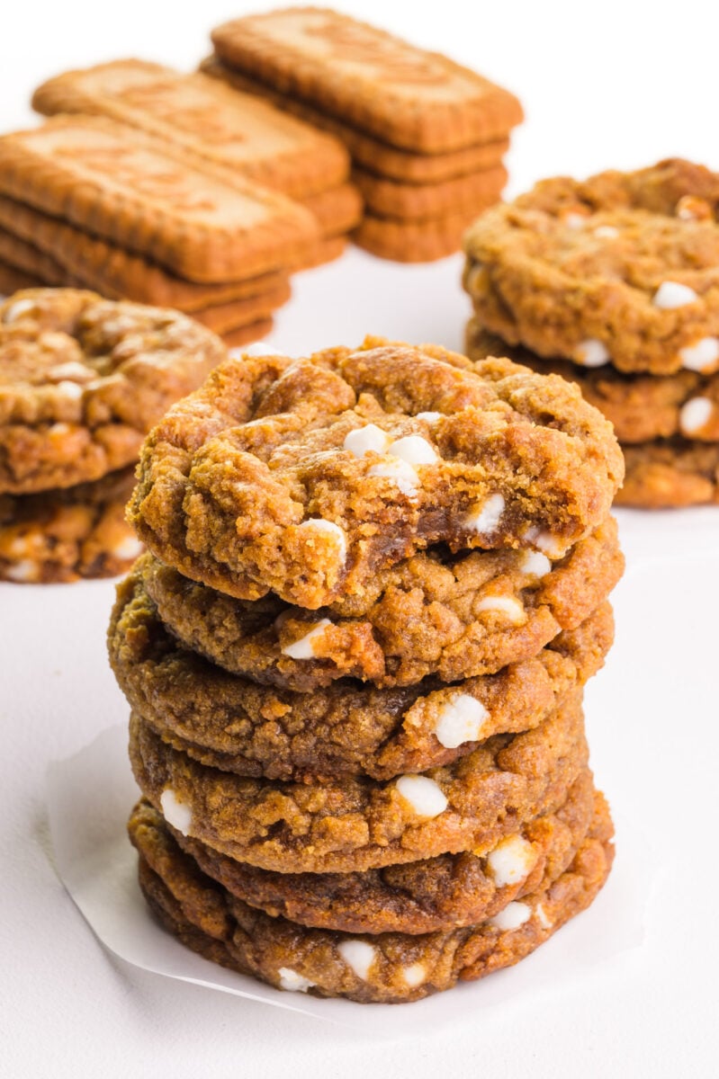 A stack of cookies has a bite taken out of the top one. There are more cookies and biscoff cookies in the background.