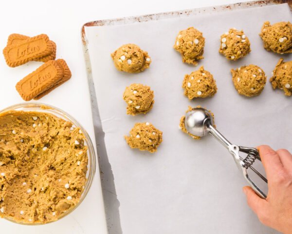 A hand holds a cookie dough dispenser pressing cookie dough balls on a baking pan.