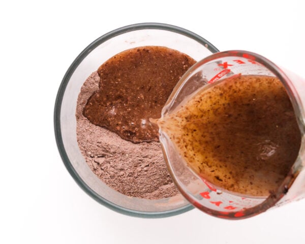 A chocolate mixture is being poured into a mixing bowl with flour and cocoa ingredients.