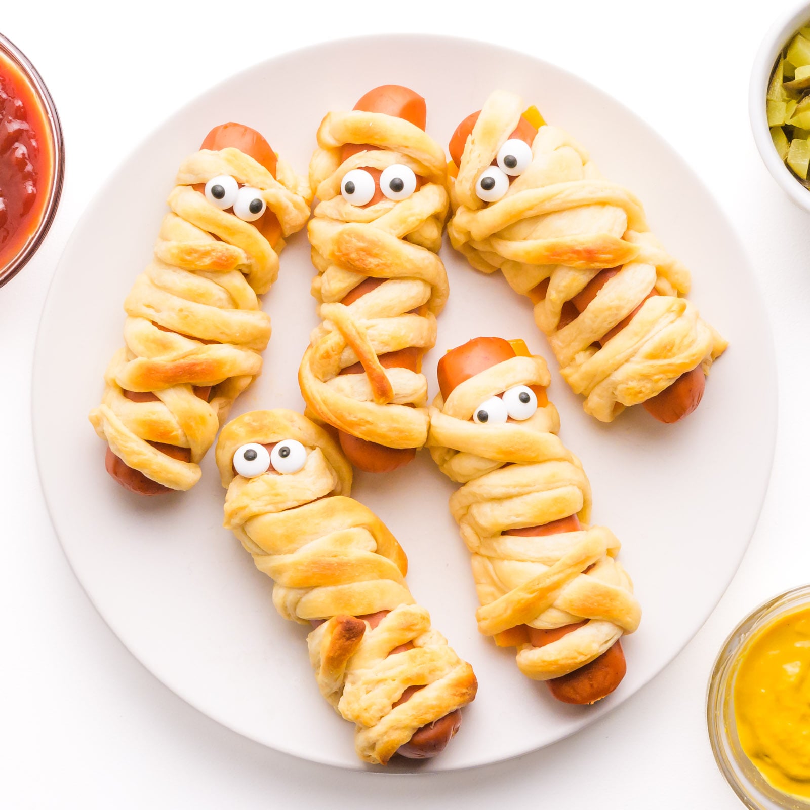 Looking down on a plate of vegan mummy dogs with candy eyes.