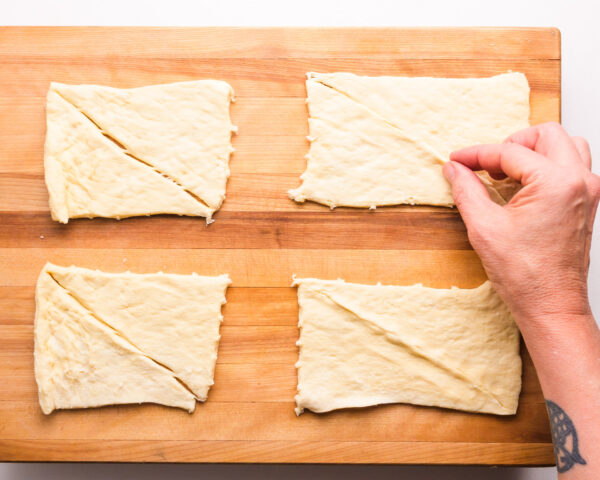 A hand is folding pieces of dough on a wooden cutting board.
