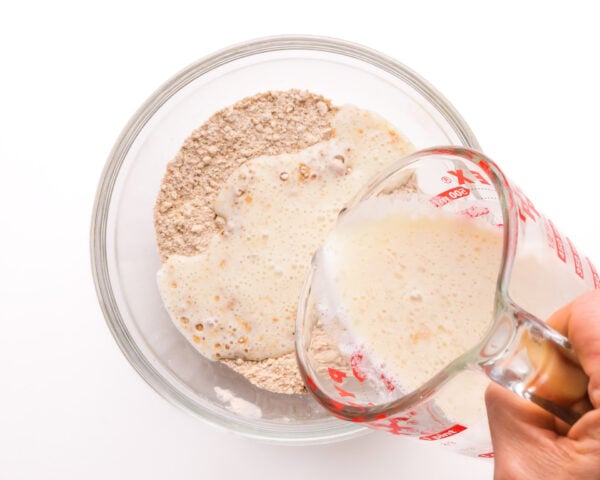 A plant-based milk mixture is being poured into a bowl with flour.