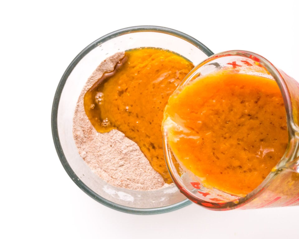 A pumpkin mixture is being poured into a bowl with flour.