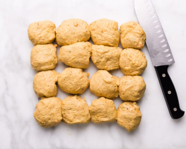 Sweet potato dough has been portioned into 16 pieces. A knife sits beside the dough pieces.