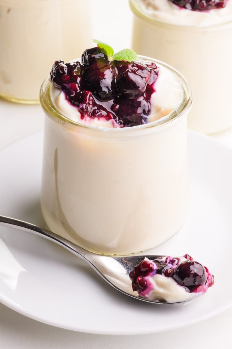 A serving dish of vegan soy yogurt has a spoonful of it sitting in front. There are two more serving dishes in the background.