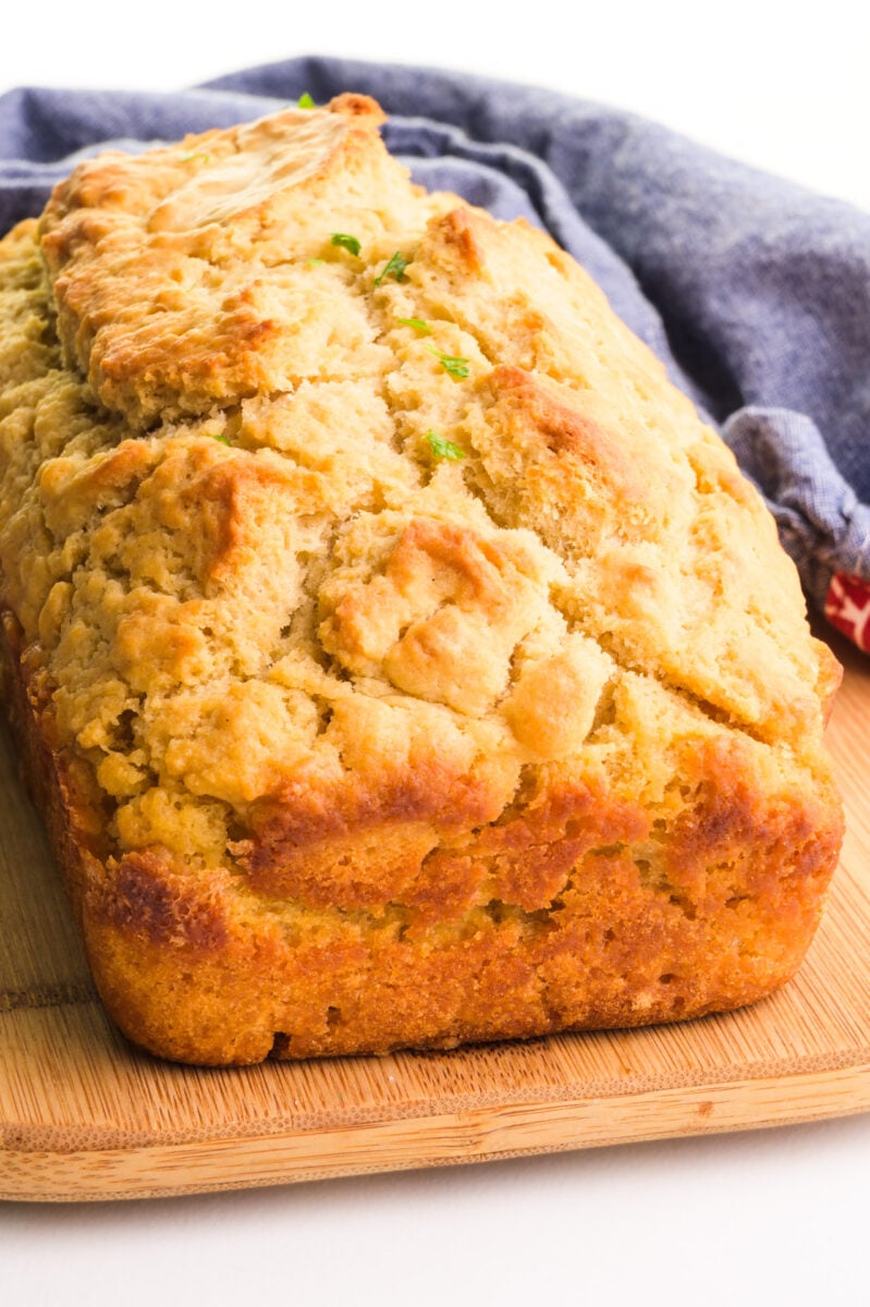 An uncut loaf of buttery beer bread sits on a cutting board in front of a blue kitchen towel.