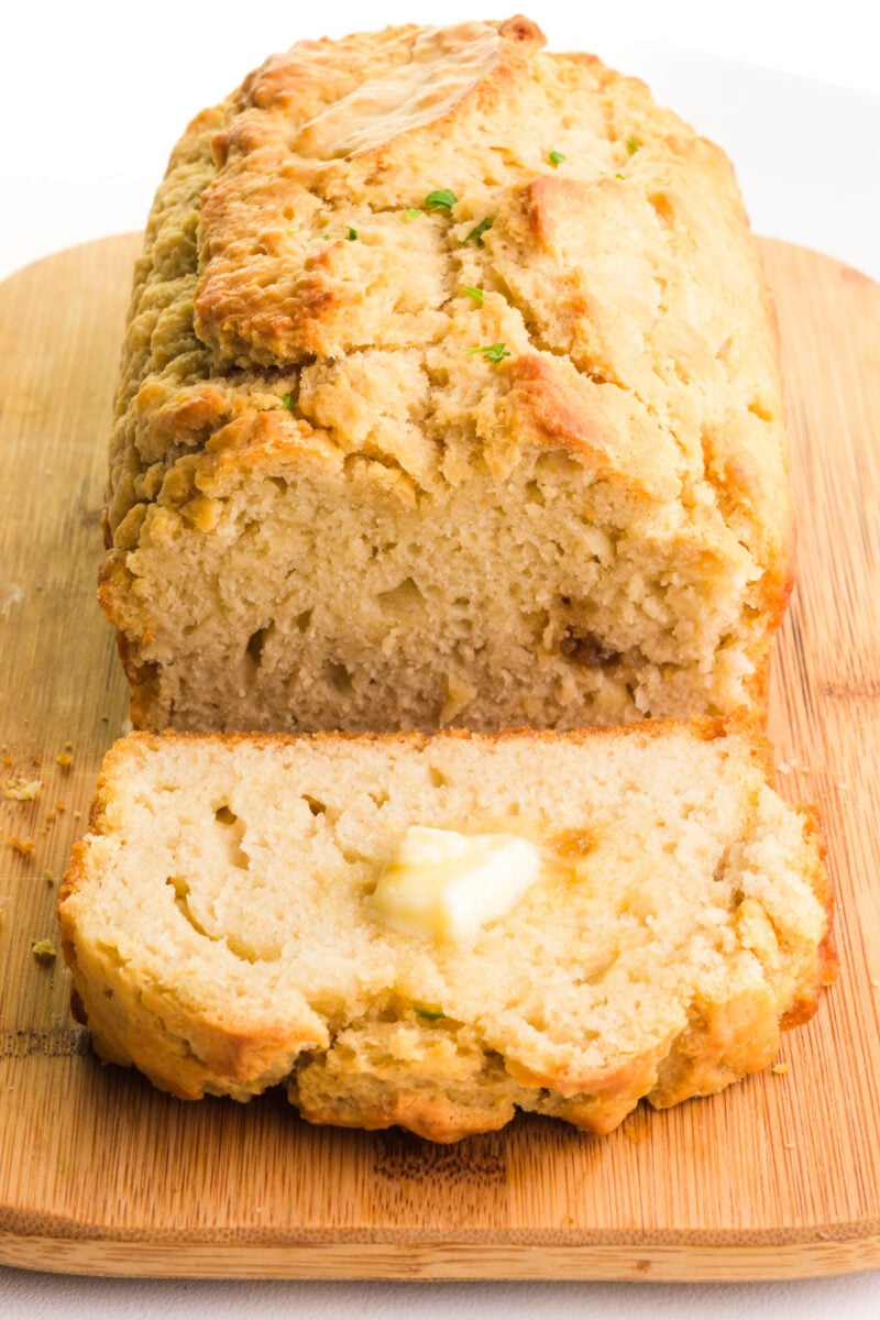 A loaf of beer bread has a slice taken out. The slice has a pat of butter on it.