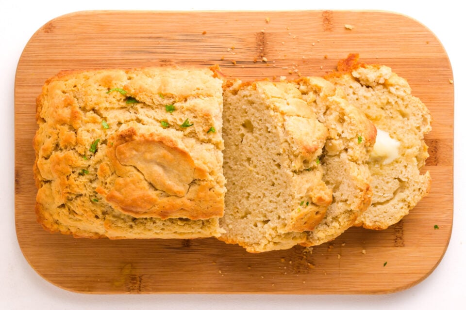Looking down on a loaf of plant-based beer bread, some of it cut into slices, on a cutting board.