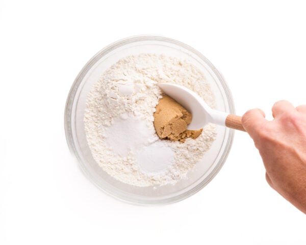 A hand stirs ingredients like flour and brown sugar in a bowl.
