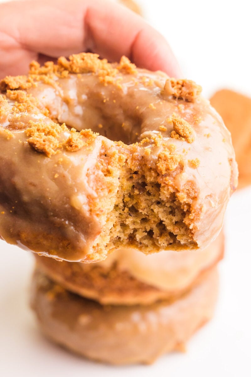 A hand holds a vegan biscoff donut with a bite taken out.
