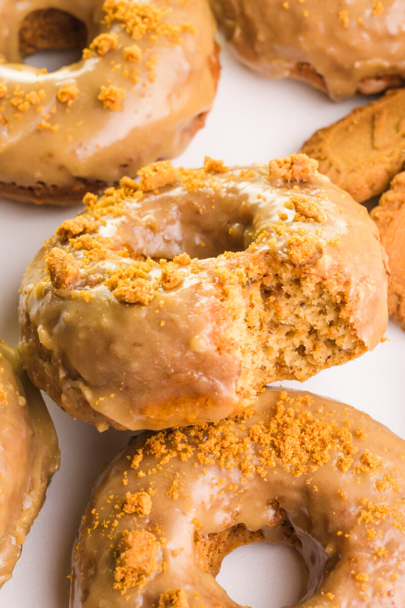 Several biscoff donuts sit on a white counter. One has a bite taken out.
