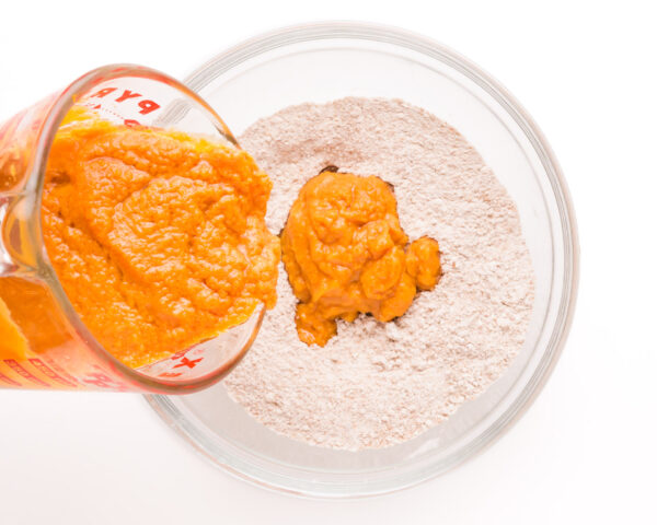 A pumpkin mixture is being poured into a bowl with flour mixture.