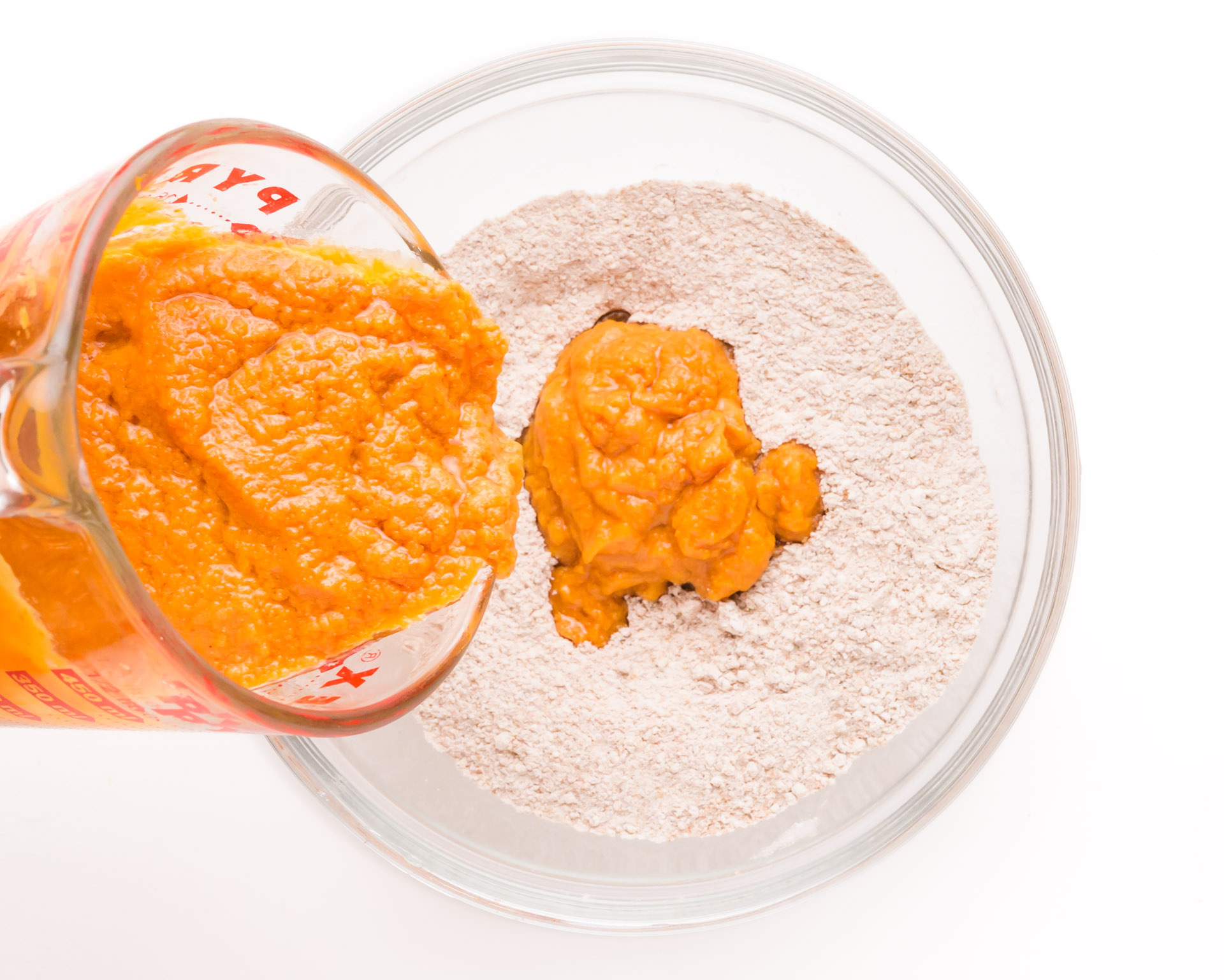 A pumpkin mixture is being poured into a bowl with flour mixture.