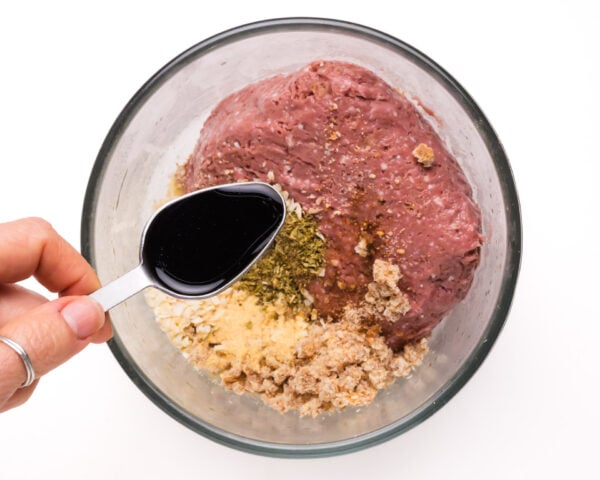 An artful pour of vegan Worcestershire sauce into a bowl filled with a tantalizing mix of Impossible Meat, breadcrumbs, and a medley of flavorful ingredients. The hands-on preparation captures the essence of crafting delicious and plant-powered Impossible Meatballs.