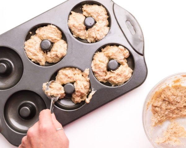 Batter is being distributed from a mixing bowl into a donut pan.
