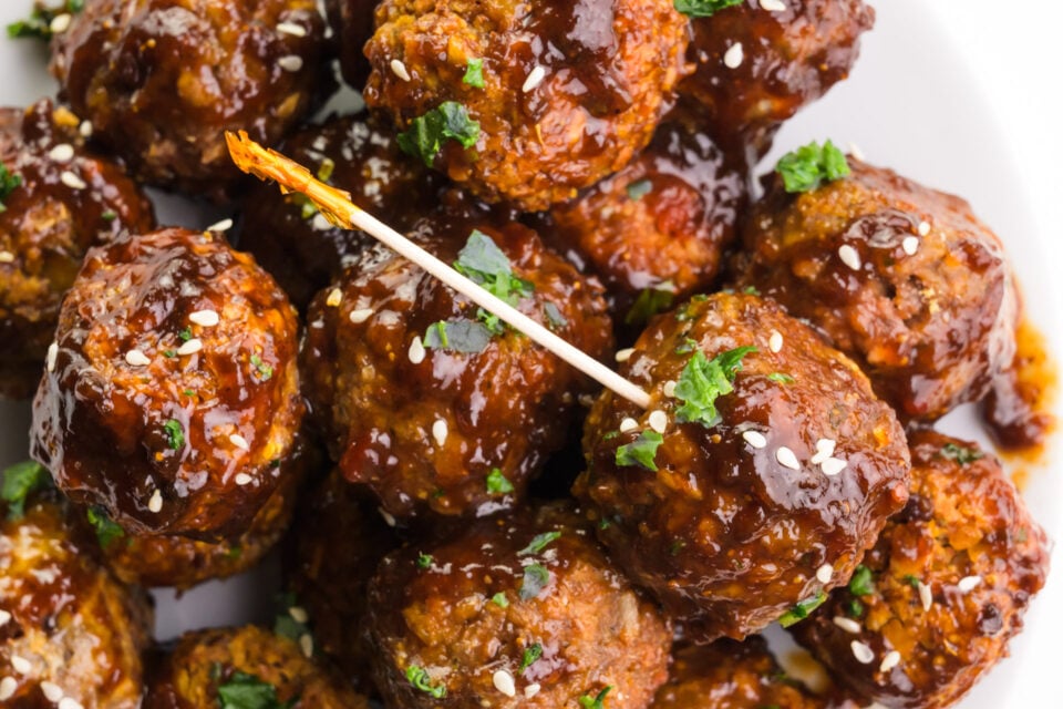 Looking down on a plate of vegan meatballs, one is skewered with a toothpick.