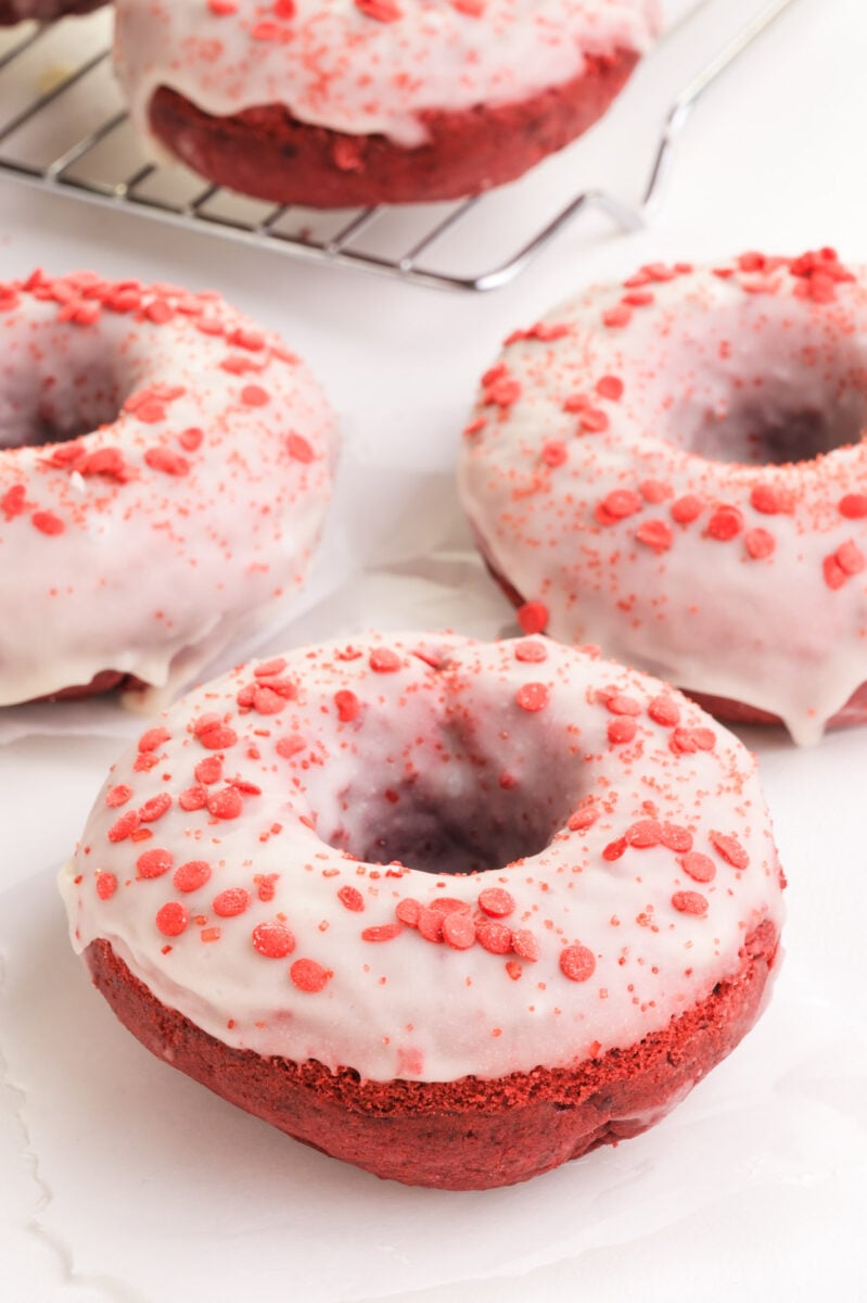 Frosted red velvet donuts are sitting on a white table.