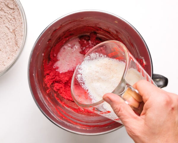 Vegan buttermilk is being poured into a batter with red cookie dough.