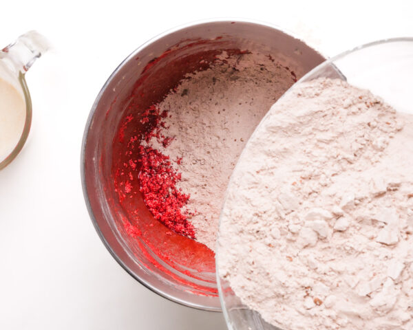 Flour is being poured into a mixing bowl with red velvet batter.