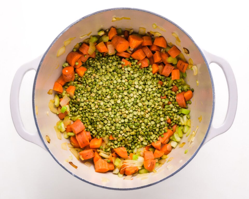Looking down on a dutch oven with split peas, chopped onions and more ingredients.