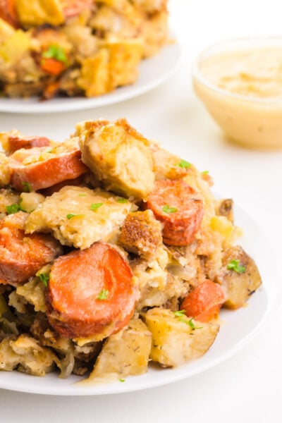 A plate of vegan Thanksgiving casserole sits in front of a bowl of gravy and more casserole in the background.