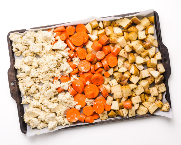Looking down on a roasting pan with potatoes, carrots, and tofu, ready to be roasted.