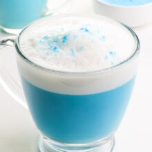 Blue matcha tea latte is in a glass mug and has steamed milk on top.