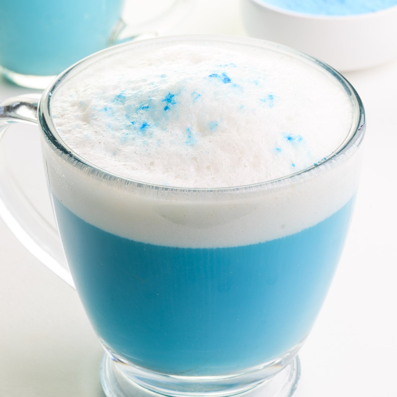 Blue matcha tea latte is in a glass mug and has steamed milk on top.