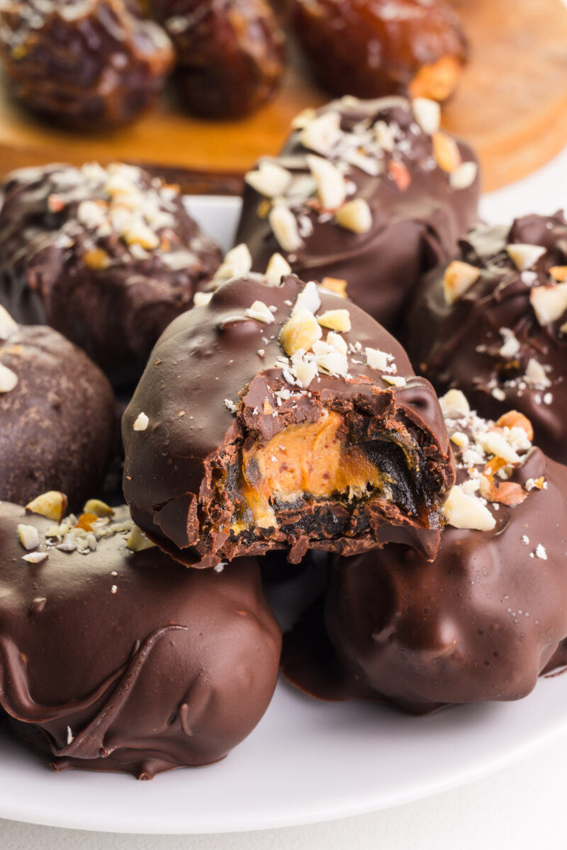 A stack of healthy snickers with dates shows the top one with a bite taken out. There are dates on a cutting board in the background.