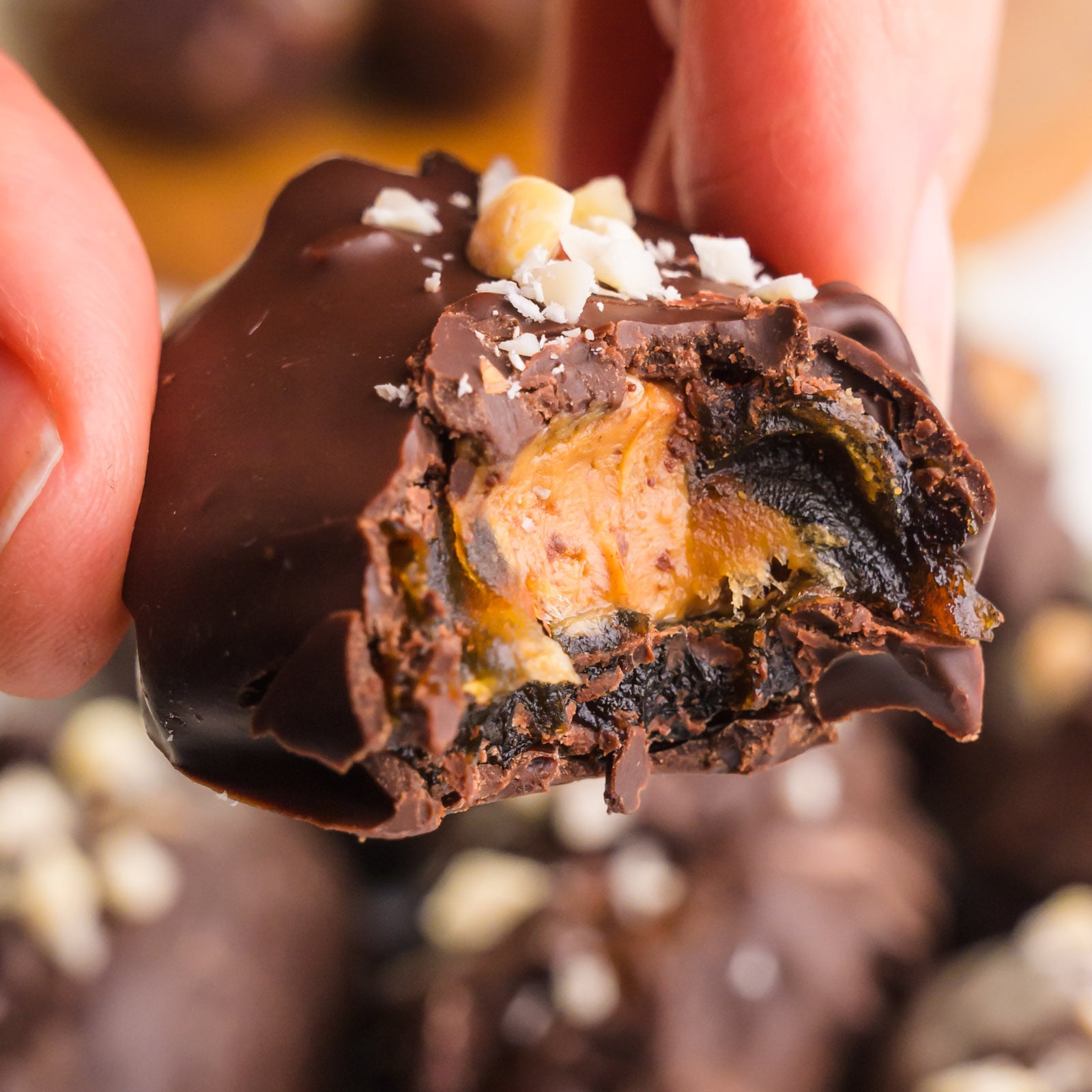 A hand holds a date snickers chocolate candy with a bite taken out, revealing peanut butter filling.