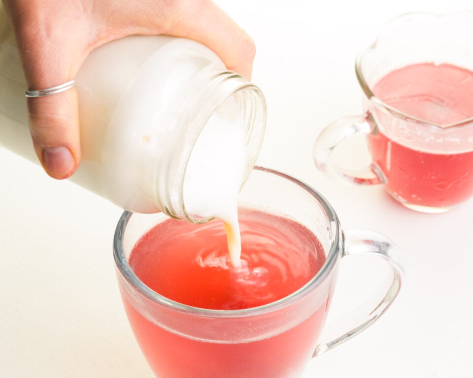 A mug being filled with steamed soy milk, creating a creamy layer atop a vibrant hot pink drink.