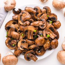 Looking down on sautéed mushrooms on a plate with whole mushrooms and a chef's knife around the plate.