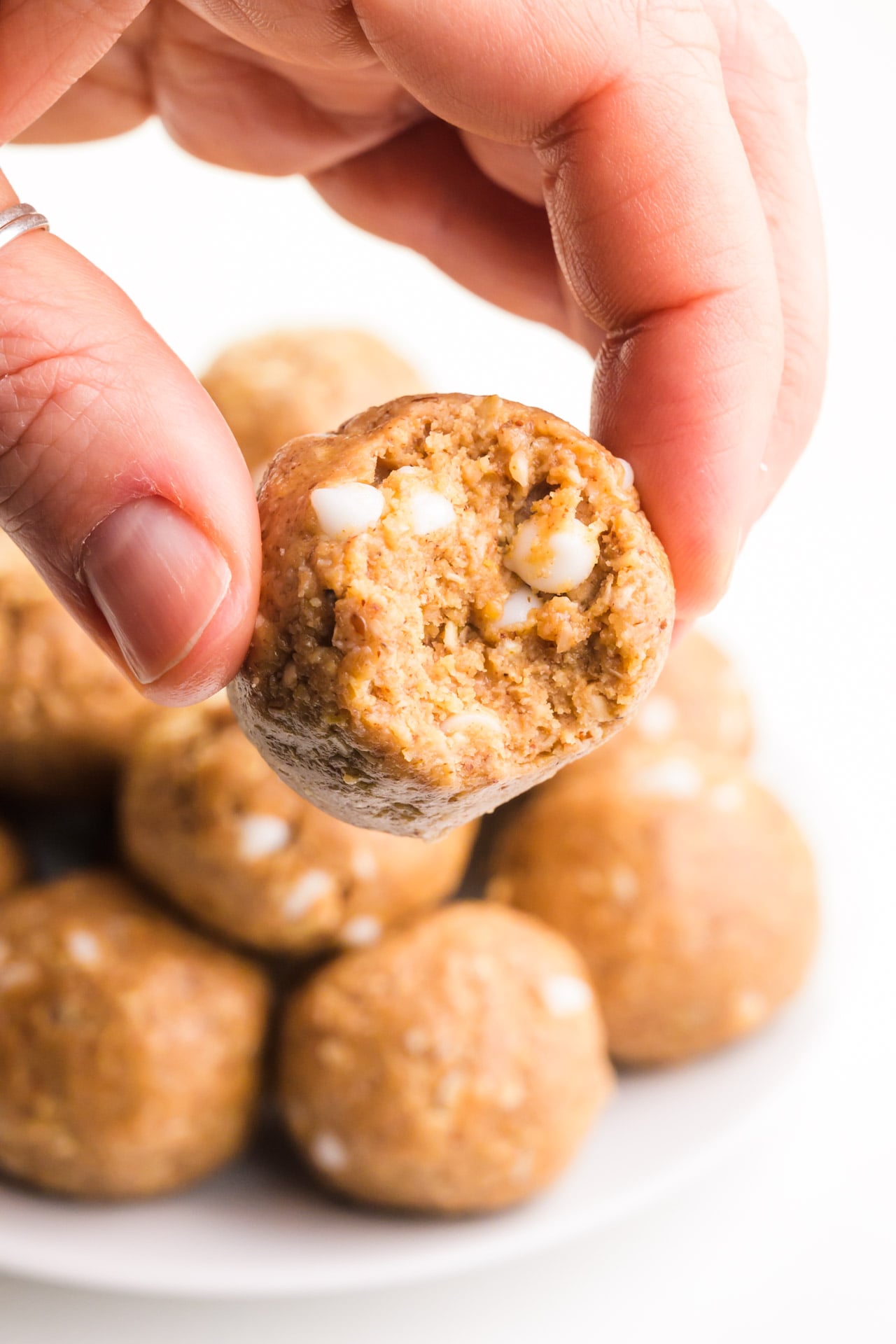 A hand holds a vanilla energy ball with a bite taken out, revealing white chocolate chips.