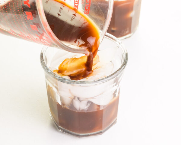 Coffee is being poured over ice in a glass.