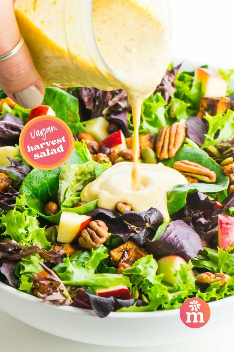 Pumpkin ranch dressing is being poured over a colorful salad. The text reads, Vegan Harvest Salad.