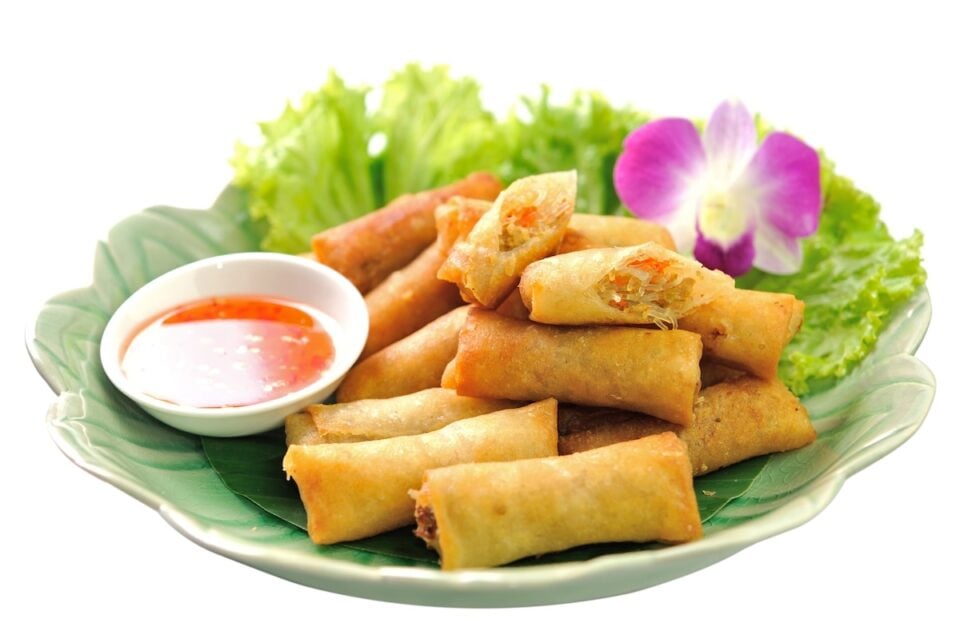 A plate of is topped with greens, fried spring rolls, dipping sauce, and a decorative flower.