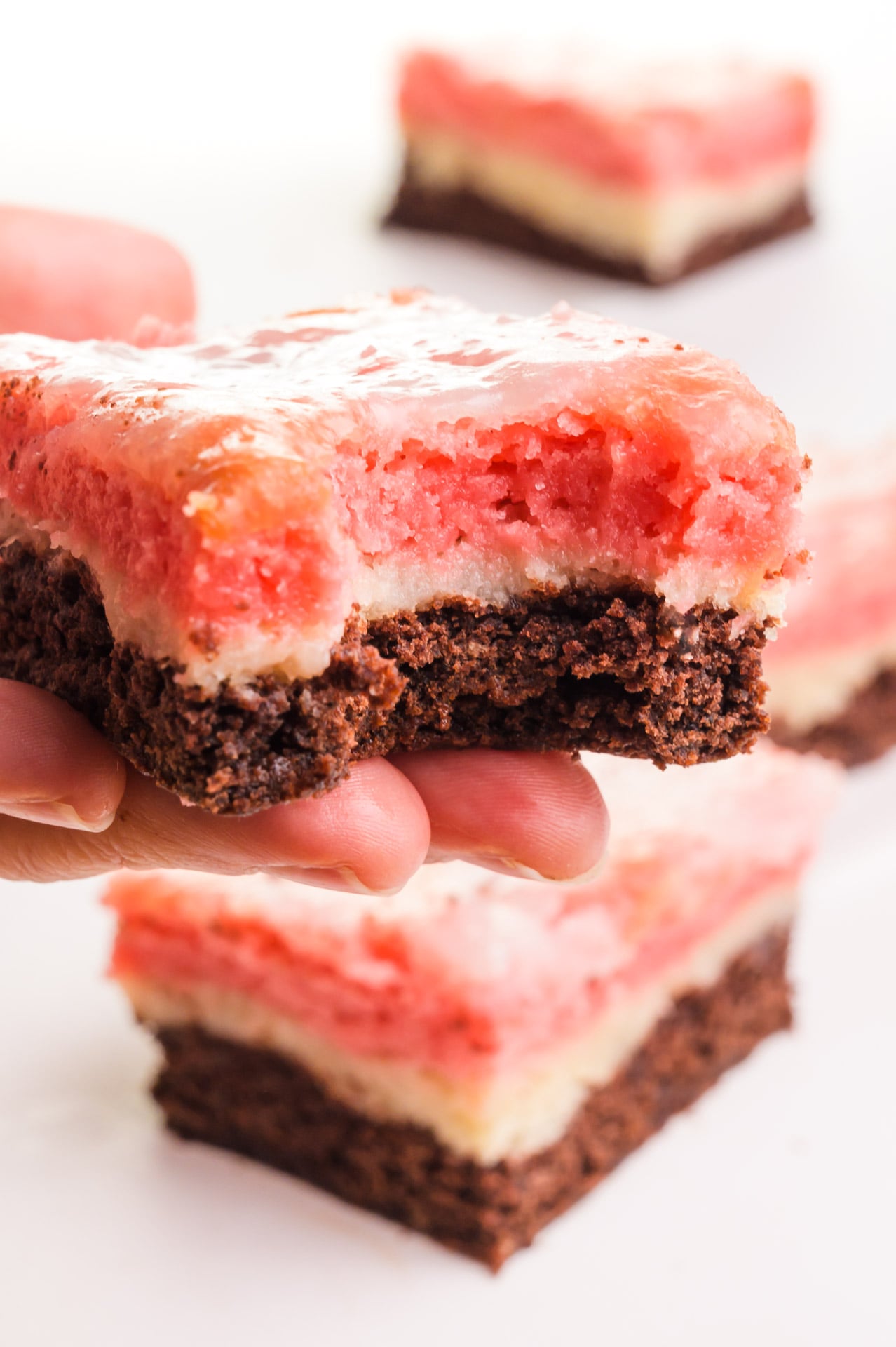 A hand holds a Neapolitan Bar with a bite taken out. There are more of the chocolate, vanilla, and strawberry treats in the background.