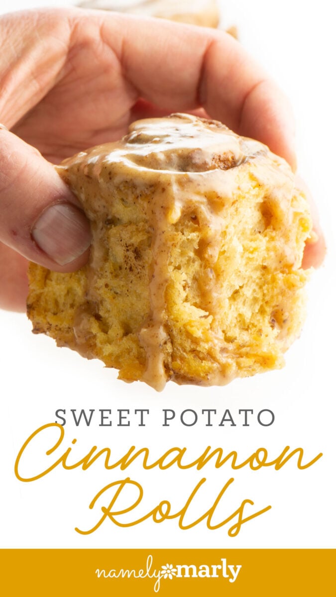 A hand holding a glazed sweet potato cinnamon roll with a soft texture.